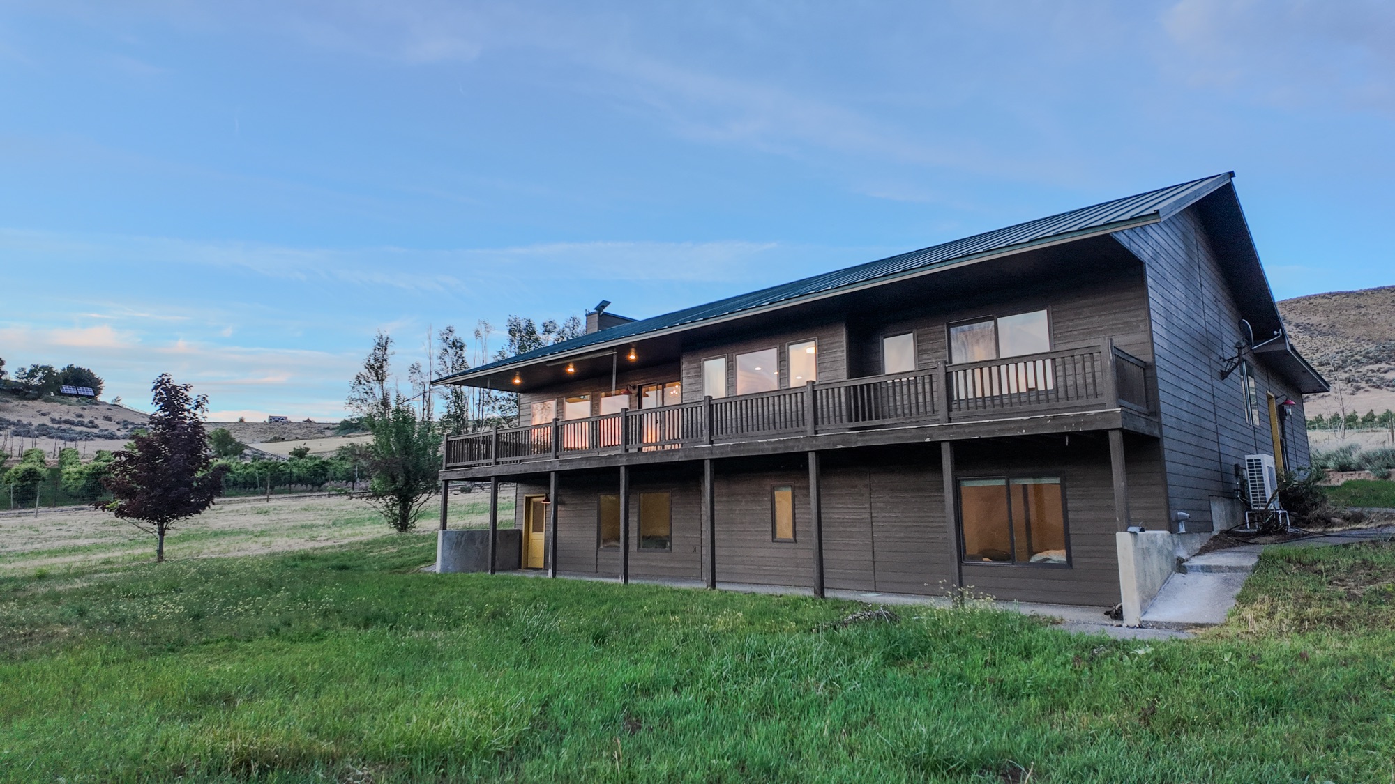 Upper deck and lower covered patio of Canyon Basin House glowing at dusk below the canyon