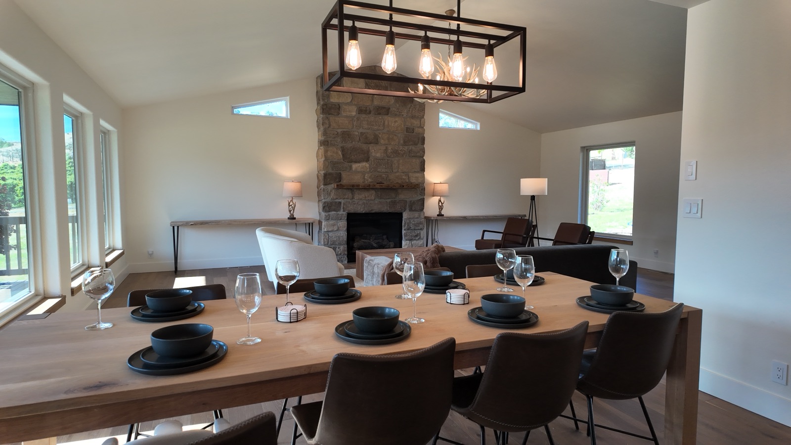 Solid white-oak dining table set for eight beside the stone fireplace and canyon-view windows