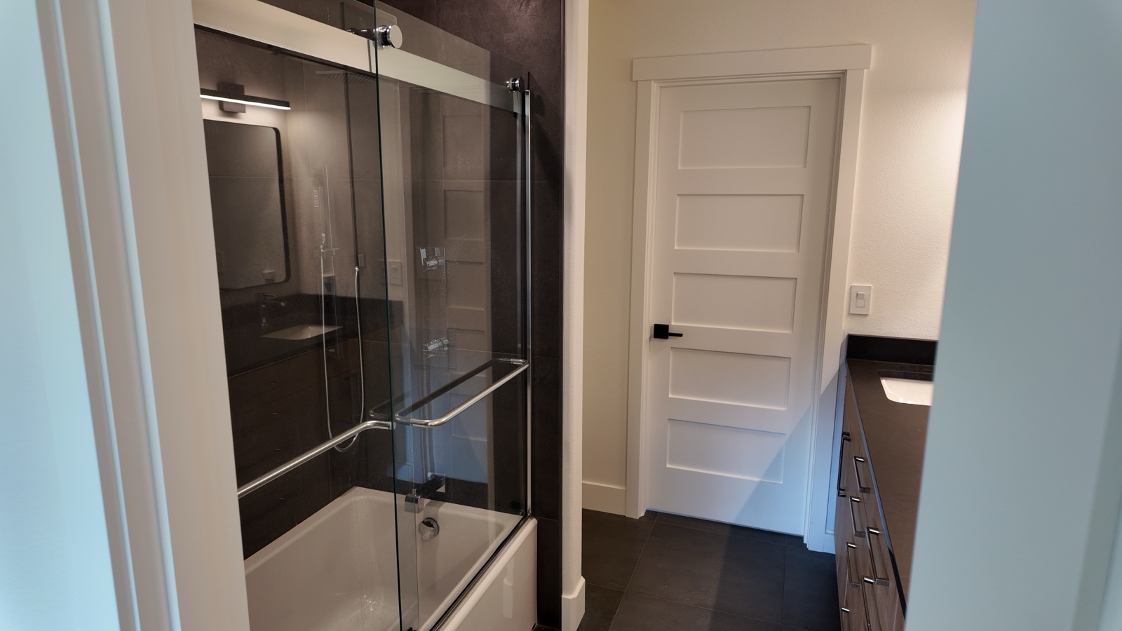 Second full bathroom with a glass tub-and-shower combo and dark tile